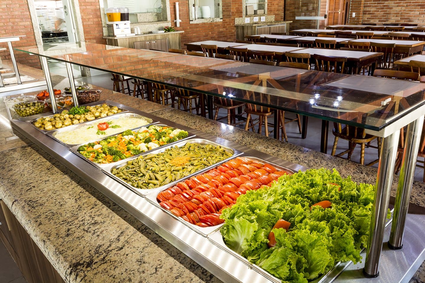 Buffet do refeitório com saladas e pratos quentes, mesas do salão ao fundo