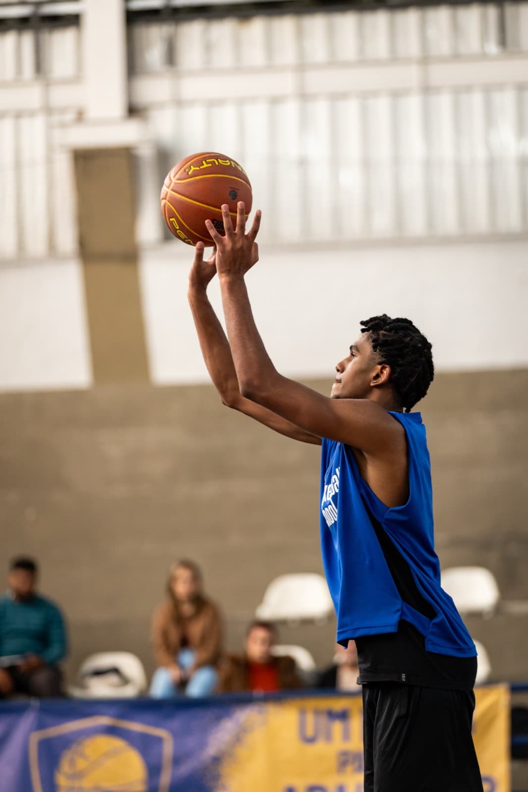 Atleta de colete azul no gesto do arremesso, bola no alto